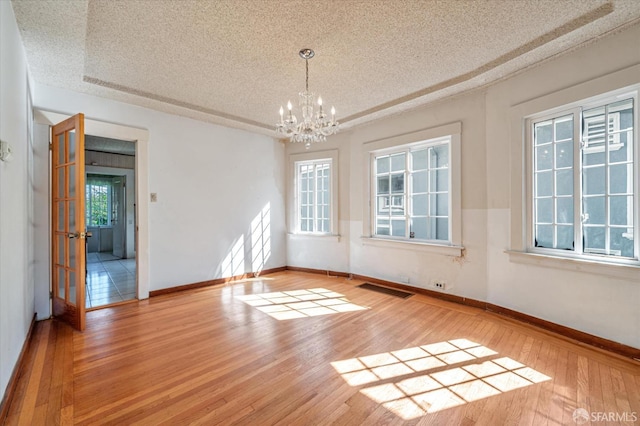 unfurnished room featuring visible vents, baseboards, hardwood / wood-style flooring, a textured ceiling, and a chandelier