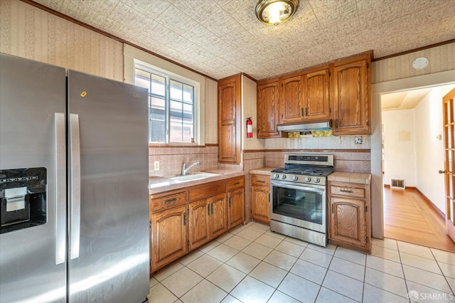 kitchen with under cabinet range hood, a sink, appliances with stainless steel finishes, tasteful backsplash, and an ornate ceiling