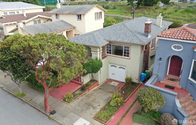 view of front of house with concrete driveway, a chimney, roof with shingles, an attached garage, and stucco siding