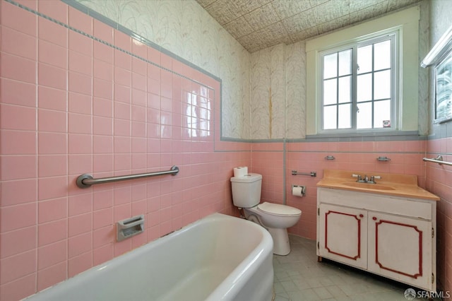 bathroom with a tub, wainscoting, toilet, and wallpapered walls