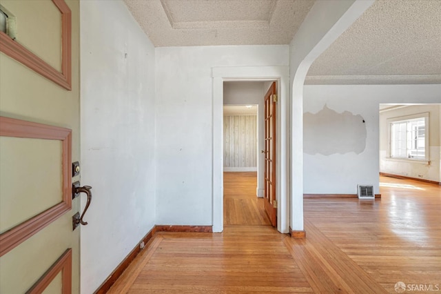 spare room with light wood finished floors, baseboards, visible vents, and a textured ceiling