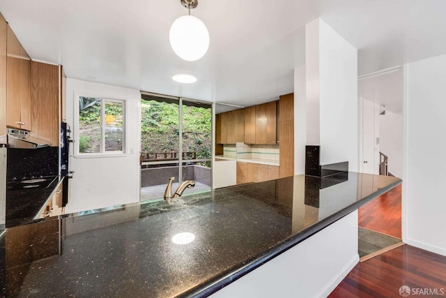 kitchen with dark hardwood / wood-style floors, range hood, hanging light fixtures, and dark stone countertops