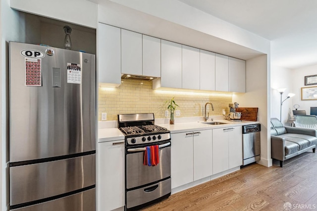 kitchen with sink, backsplash, white cabinetry, appliances with stainless steel finishes, and light wood-type flooring