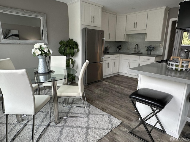 kitchen featuring dark hardwood / wood-style floors, backsplash, stainless steel refrigerator, white cabinets, and sink