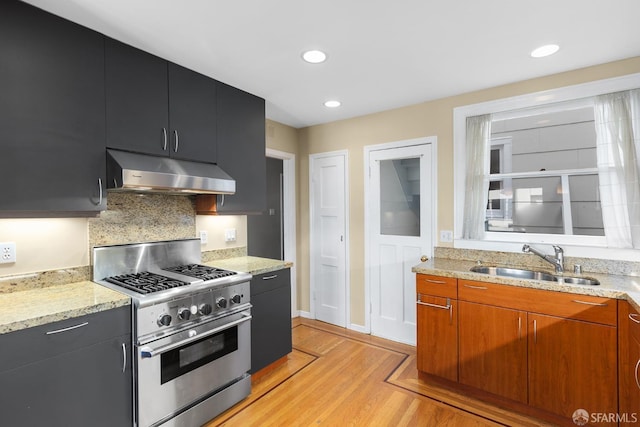 kitchen with dark cabinets, high end stainless steel range oven, a sink, and under cabinet range hood