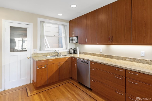 kitchen with light stone counters, recessed lighting, stainless steel appliances, a sink, and brown cabinets