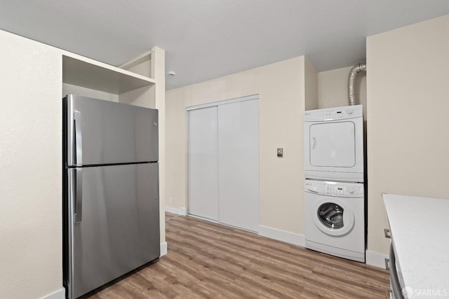 laundry area featuring stacked washer / dryer and light hardwood / wood-style flooring