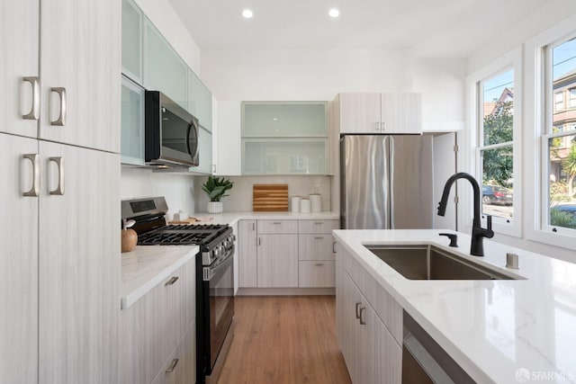 kitchen with a sink, recessed lighting, stainless steel appliances, light wood-style flooring, and light stone counters