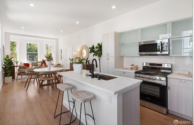 kitchen featuring a kitchen breakfast bar, light wood-style flooring, a kitchen island with sink, stainless steel appliances, and a sink