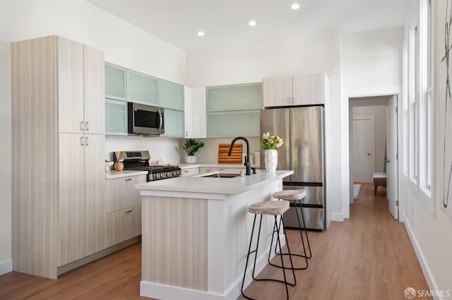 kitchen with a breakfast bar, light countertops, light wood-style floors, stainless steel appliances, and a sink