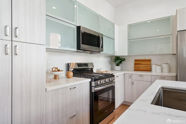 kitchen with glass insert cabinets, light stone countertops, and stainless steel appliances