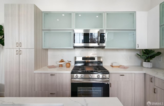 kitchen with stainless steel appliances, glass insert cabinets, backsplash, and light stone counters