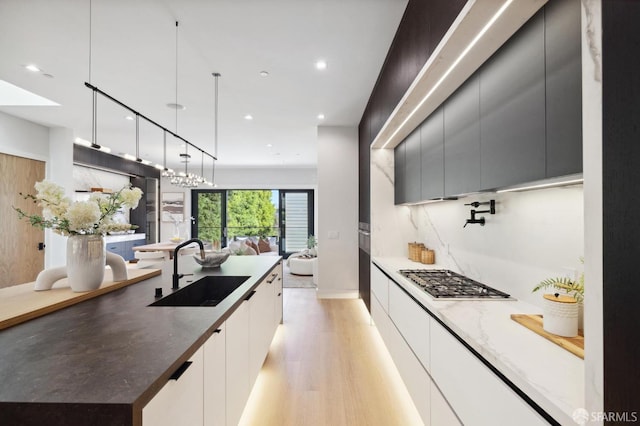 kitchen featuring stainless steel gas stovetop, sink, white cabinets, hanging light fixtures, and light wood-type flooring