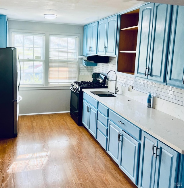 kitchen featuring stainless steel fridge, backsplash, sink, blue cabinetry, and black gas stove