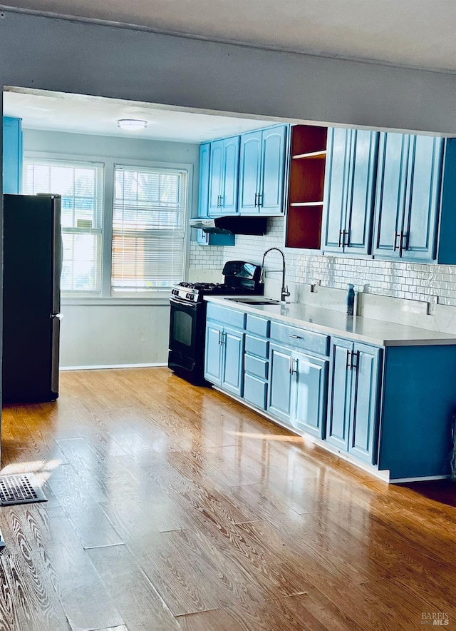 kitchen with sink, tasteful backsplash, light hardwood / wood-style flooring, blue cabinets, and black appliances