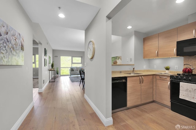 kitchen featuring light stone counters, baseboards, a sink, black appliances, and light wood-type flooring