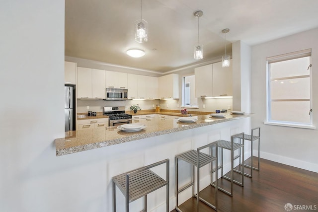 kitchen with appliances with stainless steel finishes, a peninsula, dark wood-type flooring, hanging light fixtures, and white cabinetry