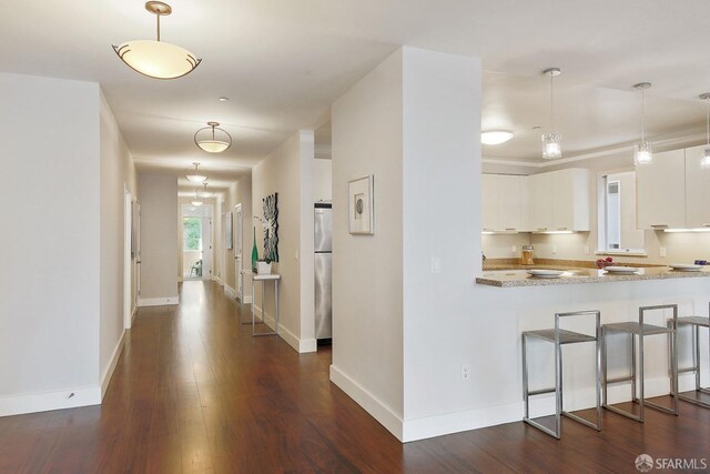 kitchen with white cabinetry, dark wood-style floors, baseboards, stainless steel fridge, and hanging light fixtures
