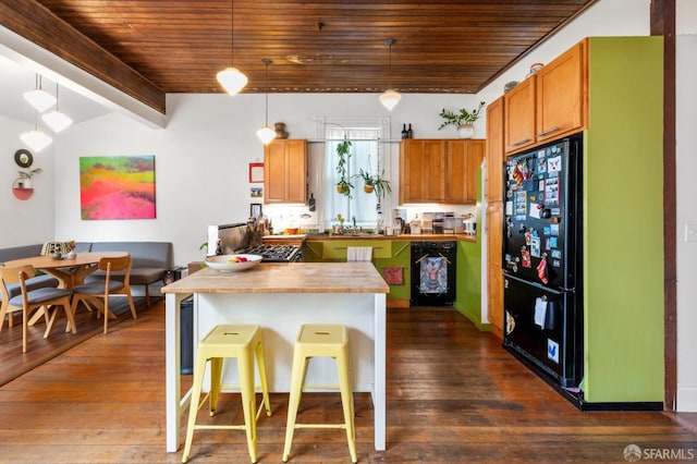 kitchen with pendant lighting, wood counters, black appliances, a kitchen breakfast bar, and beam ceiling