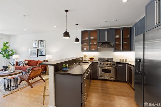 kitchen with high end appliances, kitchen peninsula, decorative light fixtures, a kitchen breakfast bar, and light wood-type flooring