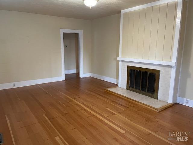 unfurnished living room featuring wood-type flooring and a brick fireplace