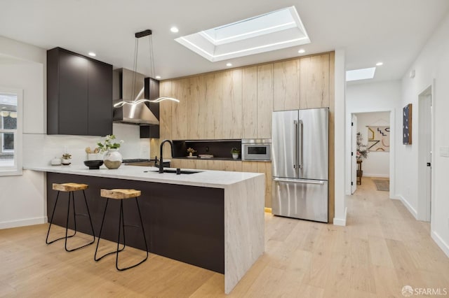 kitchen featuring high end fridge, hanging light fixtures, a skylight, kitchen peninsula, and wall chimney exhaust hood