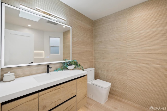 bathroom featuring vanity, toilet, a skylight, and tile walls