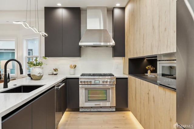 kitchen with sink, light hardwood / wood-style floors, light stone counters, stainless steel appliances, and wall chimney exhaust hood