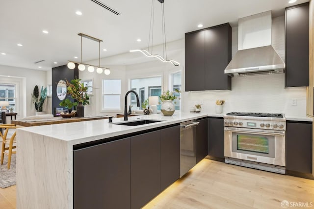 kitchen with stainless steel appliances, decorative light fixtures, sink, and wall chimney range hood