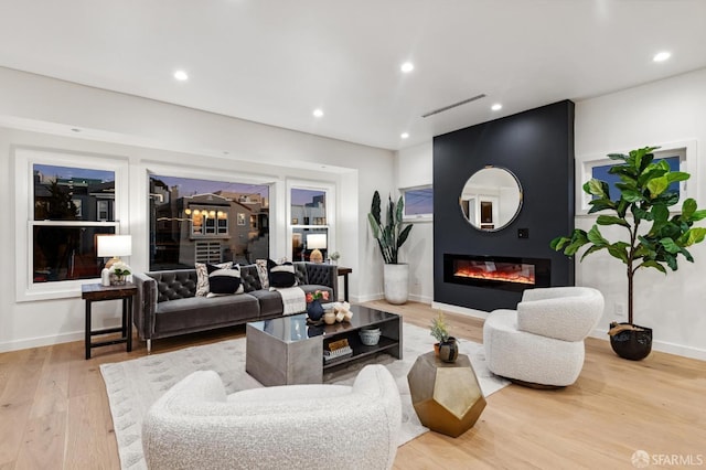 living area with a large fireplace, visible vents, baseboards, light wood-style flooring, and recessed lighting