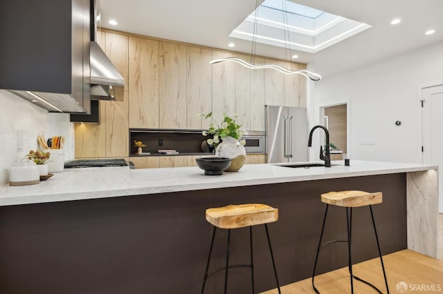 kitchen with light brown cabinetry, a skylight, sink, kitchen peninsula, and stainless steel appliances