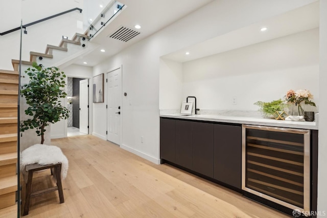 bar with wine cooler, a towering ceiling, and light hardwood / wood-style flooring