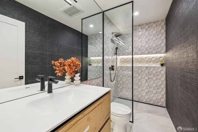 bathroom with tiled shower, vanity, toilet, and tile walls