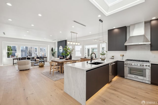 kitchen featuring a sink, wall chimney range hood, appliances with stainless steel finishes, modern cabinets, and decorative light fixtures