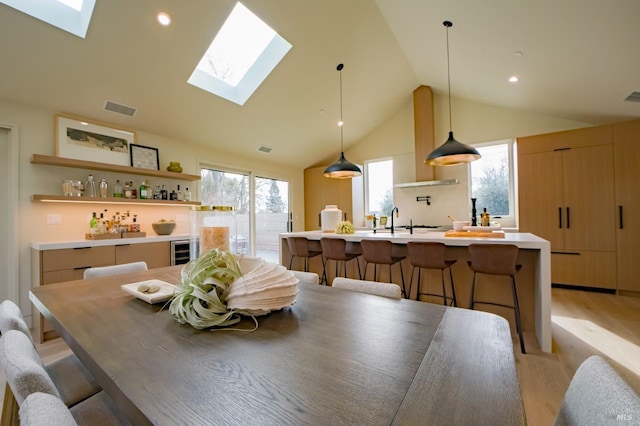 dining space featuring beverage cooler, lofted ceiling with skylight, sink, and light hardwood / wood-style flooring