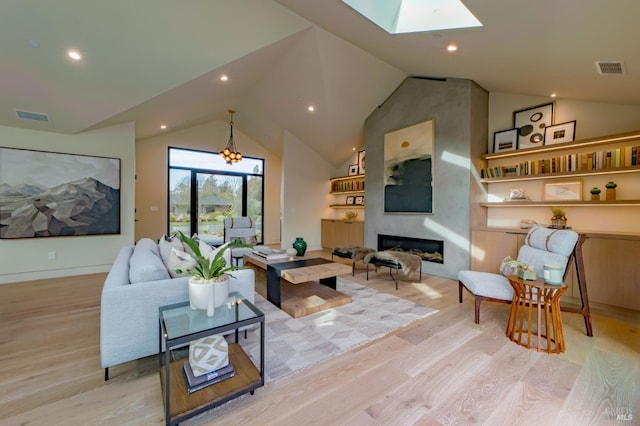 living room with a large fireplace, vaulted ceiling with skylight, and light wood-type flooring