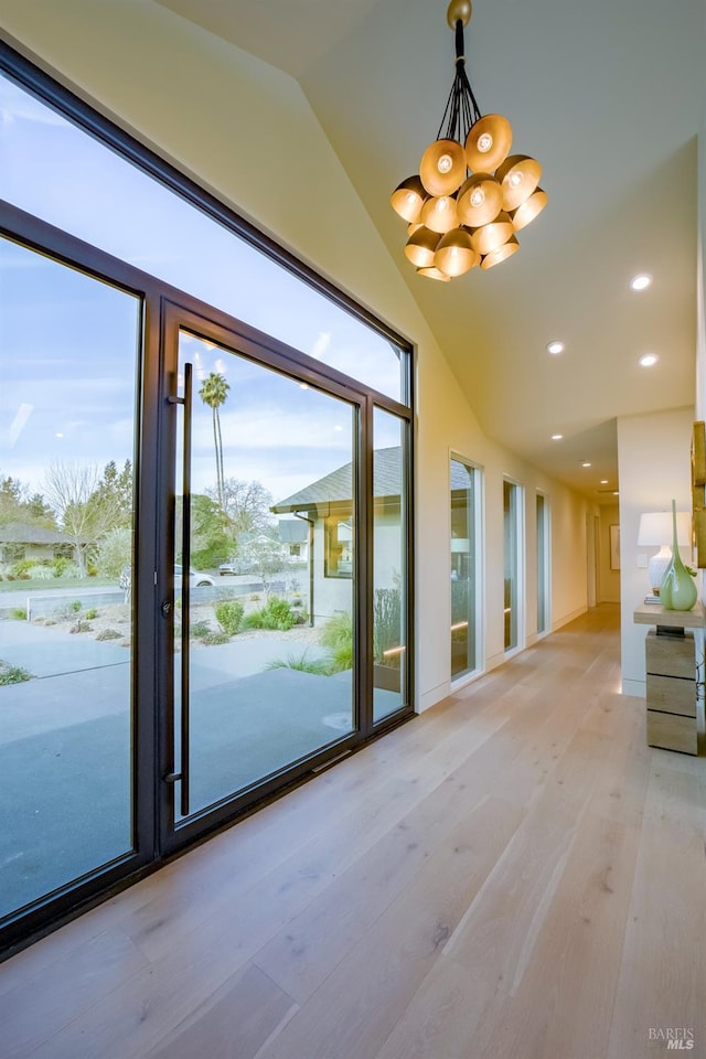 entryway with an inviting chandelier, vaulted ceiling, and light wood-type flooring