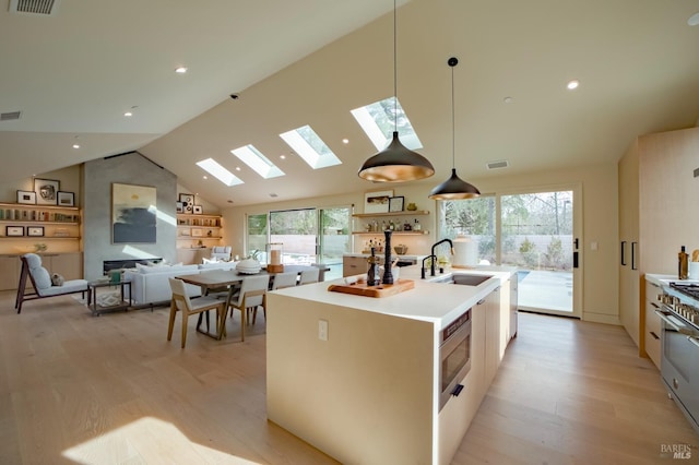 kitchen featuring pendant lighting, sink, lofted ceiling, a center island with sink, and light wood-type flooring