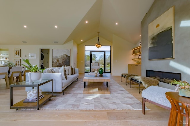 living room with stacked washer and clothes dryer, lofted ceiling, and light hardwood / wood-style floors