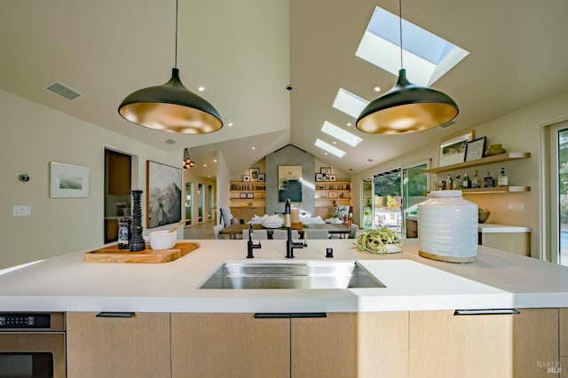 kitchen with pendant lighting, sink, vaulted ceiling with skylight, light brown cabinetry, and oven