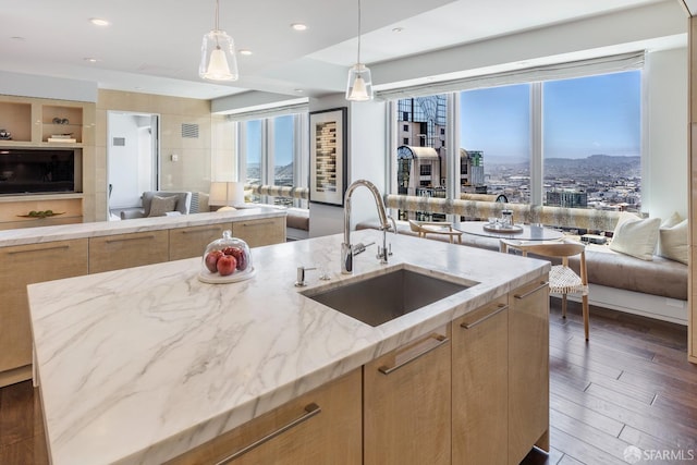 kitchen featuring a kitchen island with sink, sink, dark hardwood / wood-style floors, light brown cabinetry, and light stone counters