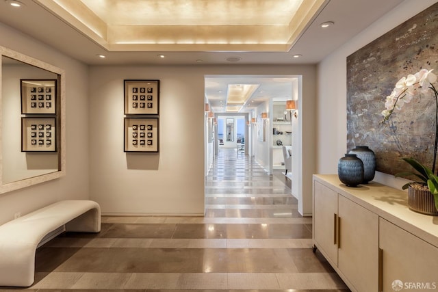 corridor with light tile patterned floors and a tray ceiling