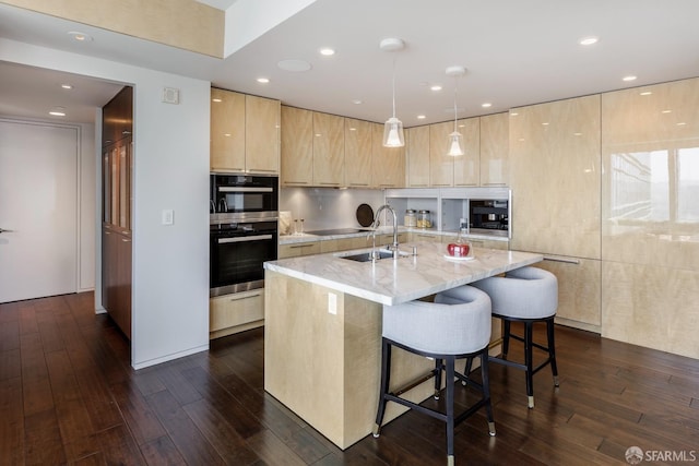 kitchen with sink, hanging light fixtures, light stone counters, an island with sink, and light brown cabinetry