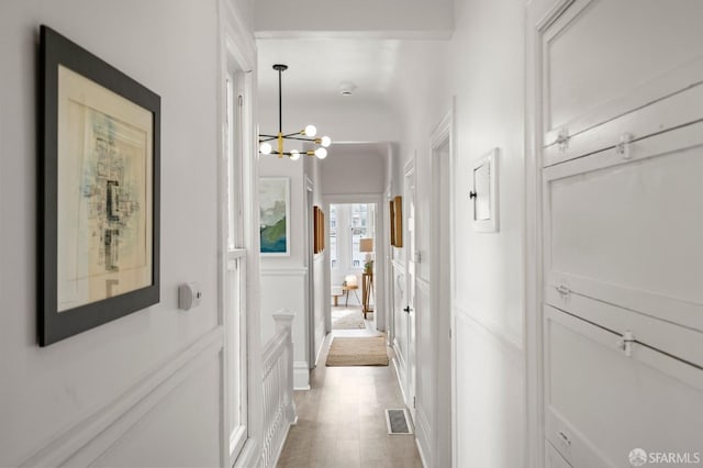 hallway with visible vents, a decorative wall, light wood-style flooring, and a notable chandelier