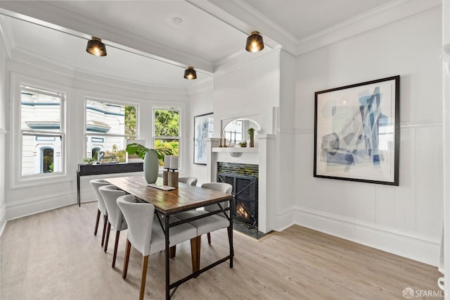 dining space featuring ornamental molding, light wood-style flooring, a decorative wall, and a lit fireplace