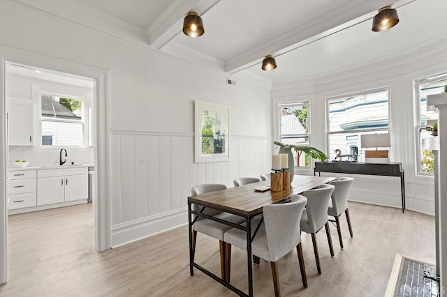 dining room with light wood-style flooring, a wainscoted wall, a healthy amount of sunlight, and beamed ceiling