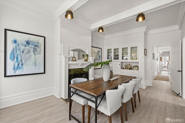 dining area featuring a decorative wall, ornamental molding, and light wood-style floors