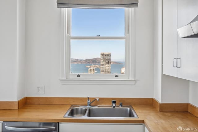 kitchen featuring sink, dishwasher, white cabinets, wood counters, and wall chimney exhaust hood