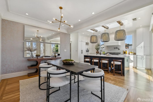 dining room featuring a notable chandelier, light hardwood / wood-style flooring, ornamental molding, and sink