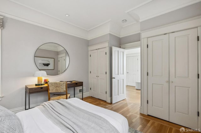 bedroom featuring ornamental molding, light hardwood / wood-style floors, and two closets